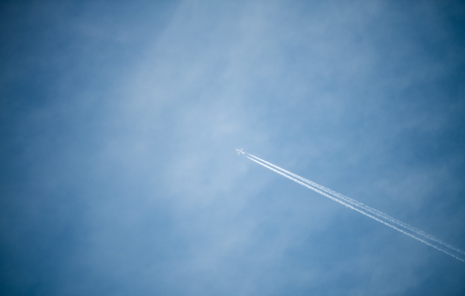 A jet crossing a wide blue sky, twin contrails trailing to the corner of the frame
